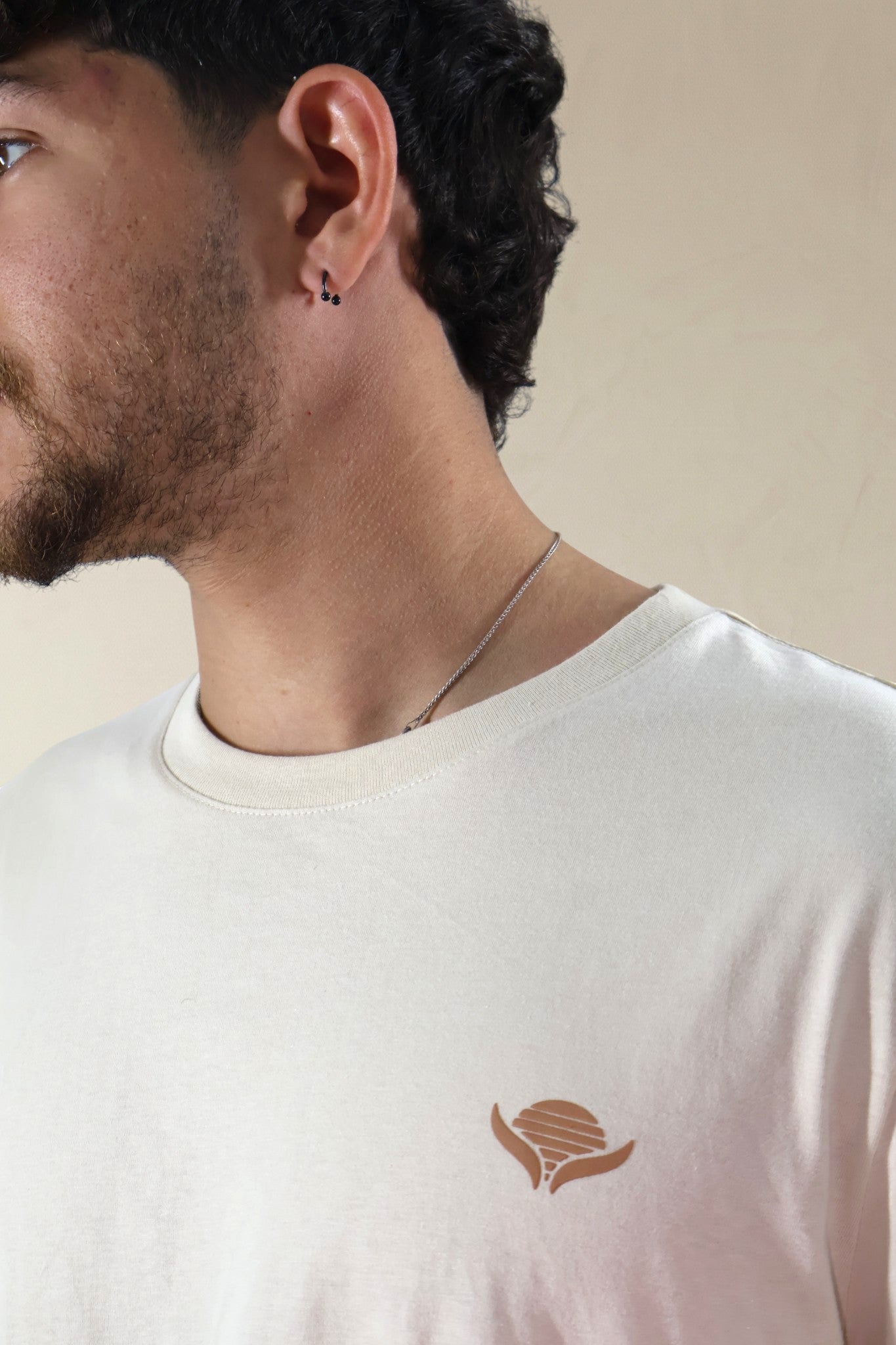 Man wearing a white t-shirt with a logo on a beige background