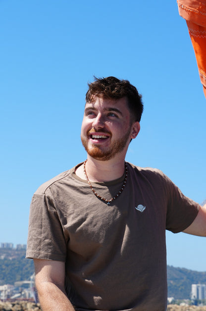 Man with a beard and short hair wearing a brown t-shirt against a blue sky.