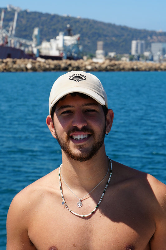 Man wearing a cap and no shirt by a body of water with a cityscape in the background