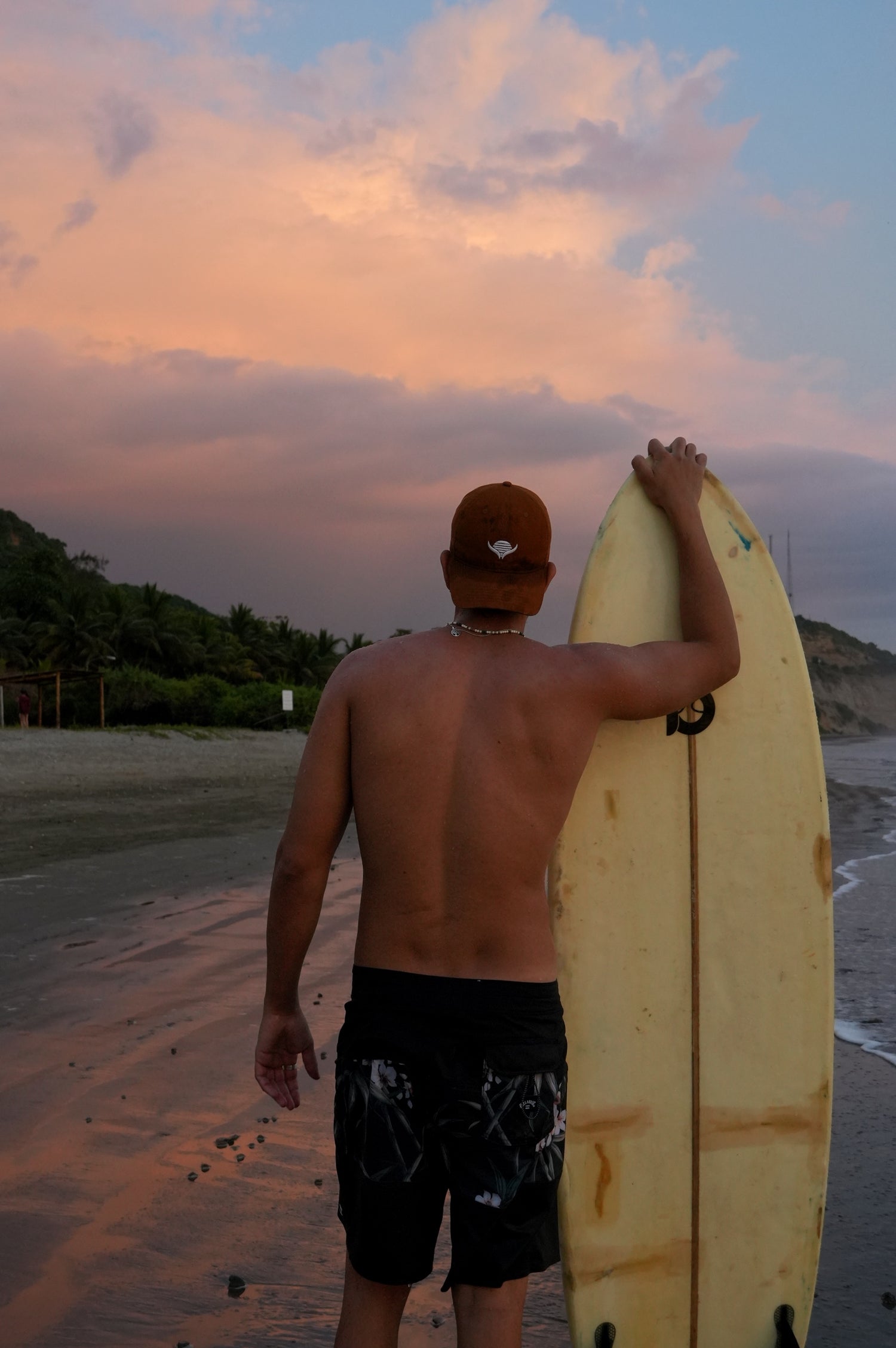 Man holding a surfboard on a beach at sunset