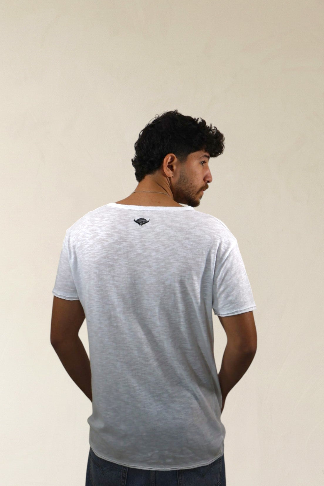 Man wearing a white t-shirt with a small logo on the back, standing against a plain background