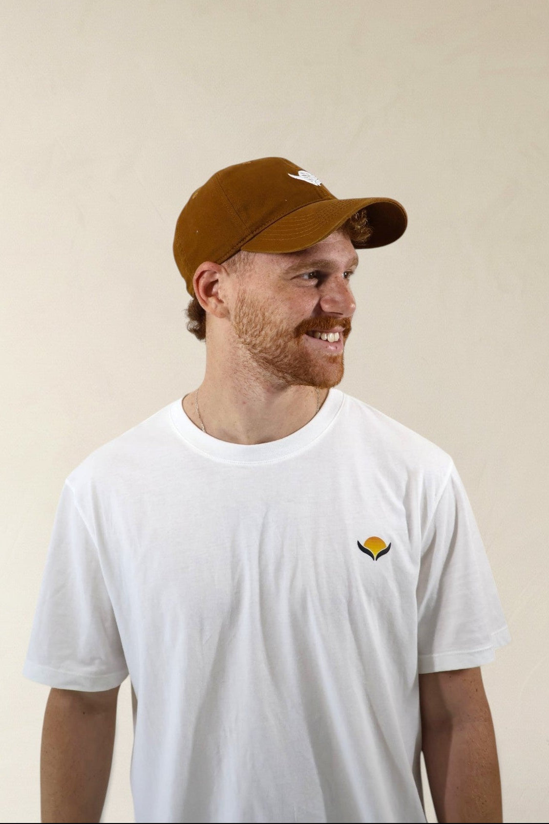 Man wearing a brown cap and white t-shirt with a logo on a beige background