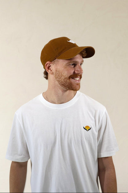 Man wearing a brown cap and white t-shirt with a logo on a beige background