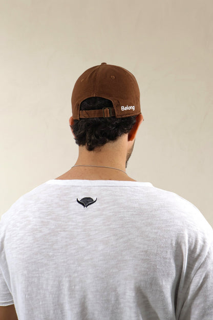 Person wearing a brown cap with 'Belong' logo and white t-shirt with black logo on beige background