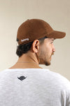 Man wearing a brown cap with 'Belong' text and a white t-shirt with a black logo on a beige background
