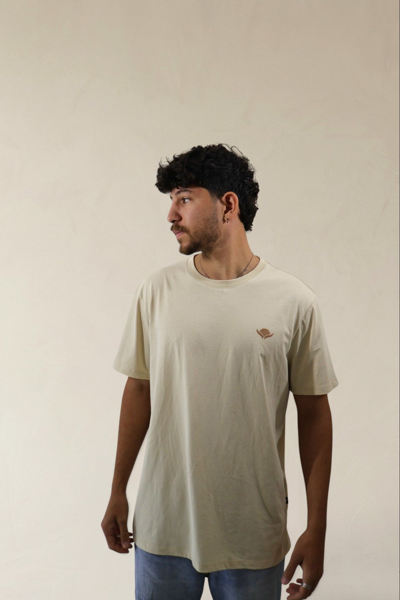 Man wearing a beige t-shirt with a small logo on a plain background