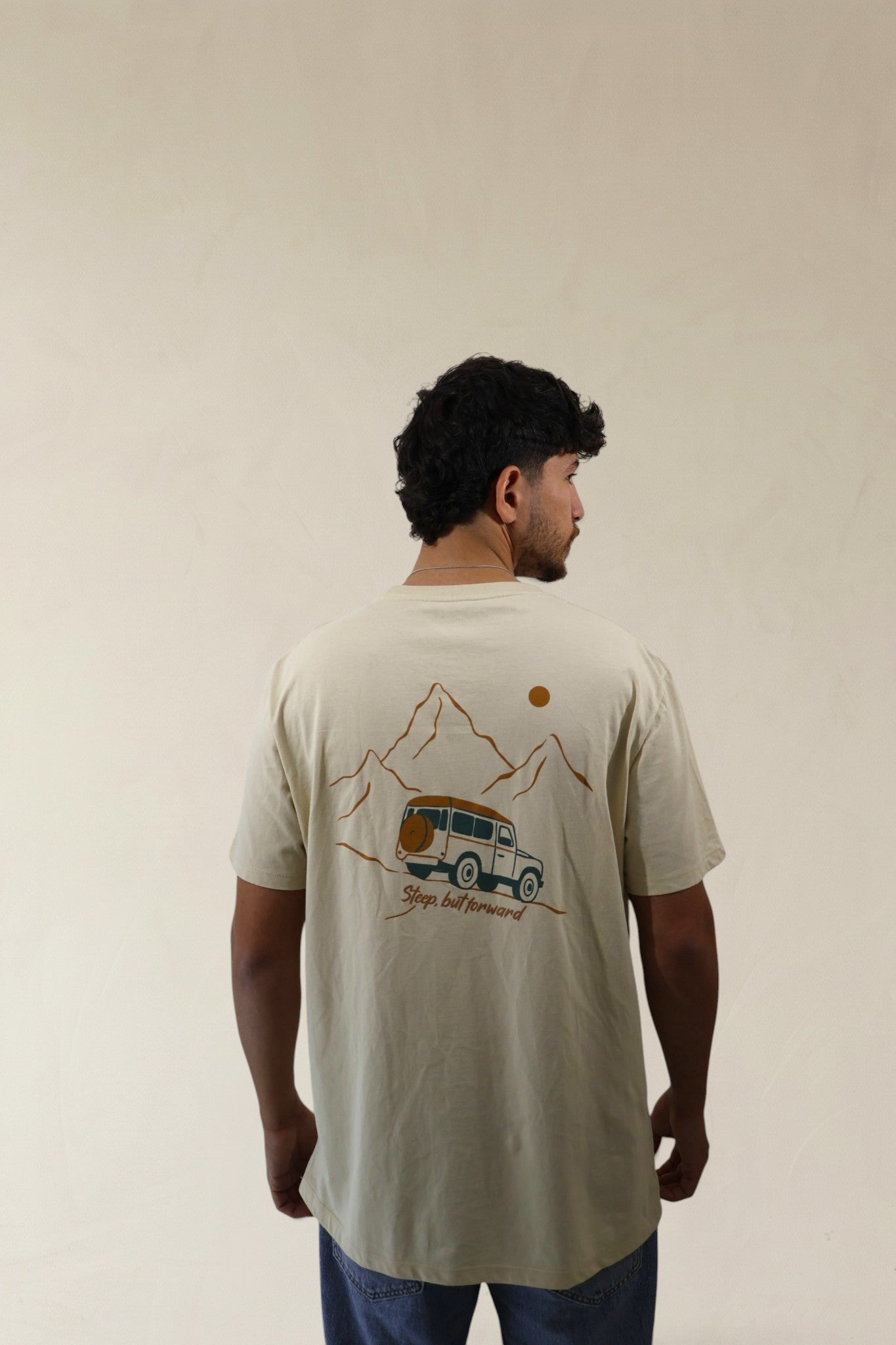 Man wearing a beige t-shirt with a graphic design on the back, standing against a plain background