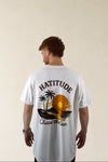 Person wearing a white t-shirt with a graphic design and text on the back, standing against a beige background.
