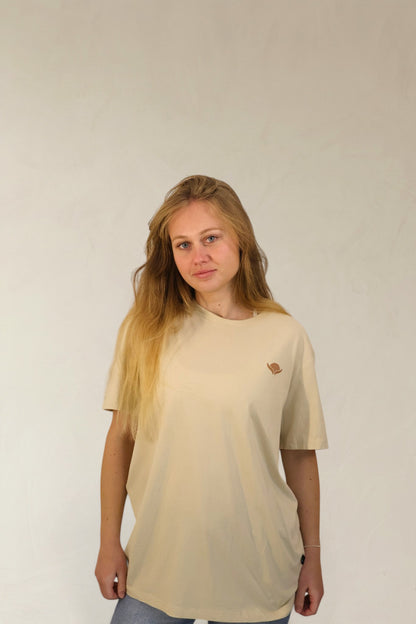 Woman wearing a beige t-shirt with a small logo on a plain background