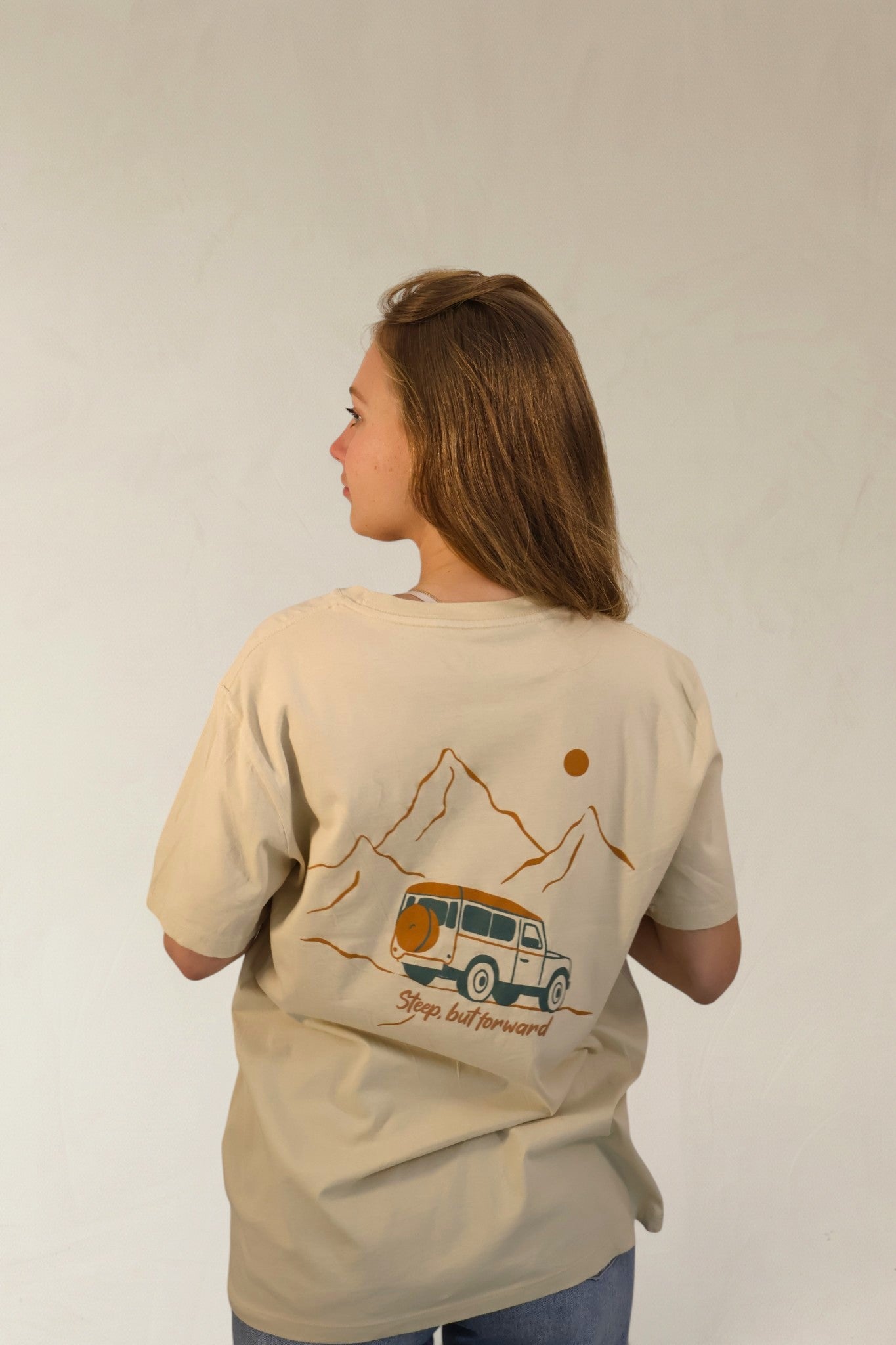 Person wearing a beige t-shirt with a graphic design on the back