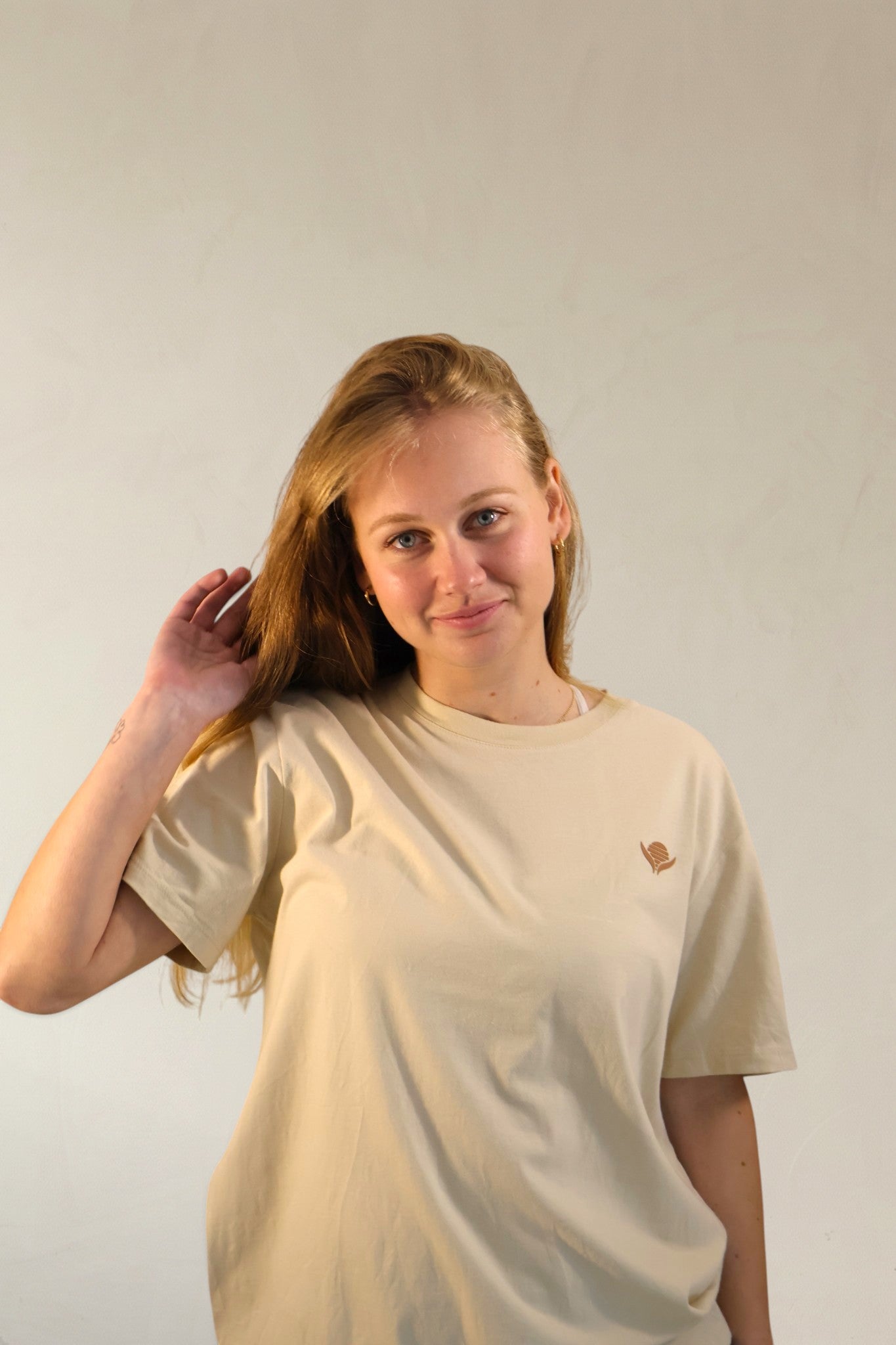 Person wearing a beige t-shirt with a small logo on a plain background